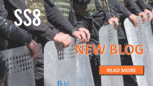 A line of police officers in riot gear holding large metal shields.
