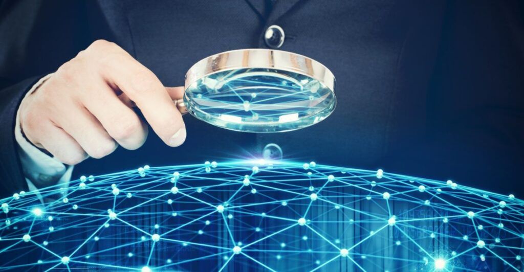 A hand holding a magnifying glass over a digital network of connected dots in the shape of a globe