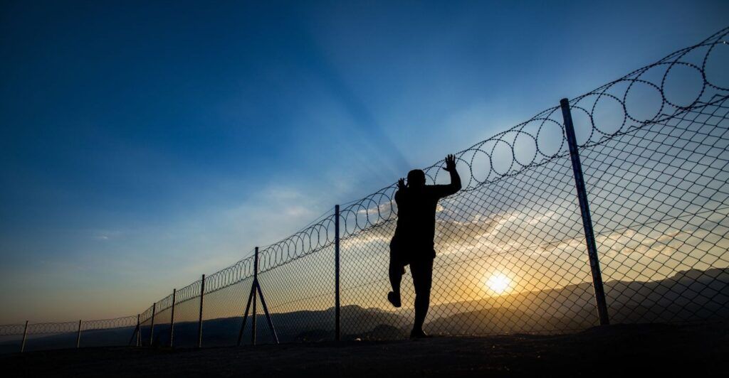 A man climbing a fence with rings of barbed wire on top.