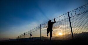 A man climbing a fence with rings of barbed wire on top.
