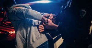 A police officer handcuffing a man in a grey sweatshirt.