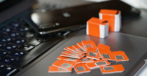 Piles of orange SIM cards and a mobile phone resting on an open laptop