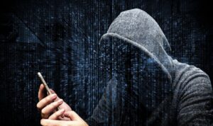 A hooded figure with a hidden face looking at a mobile phone.