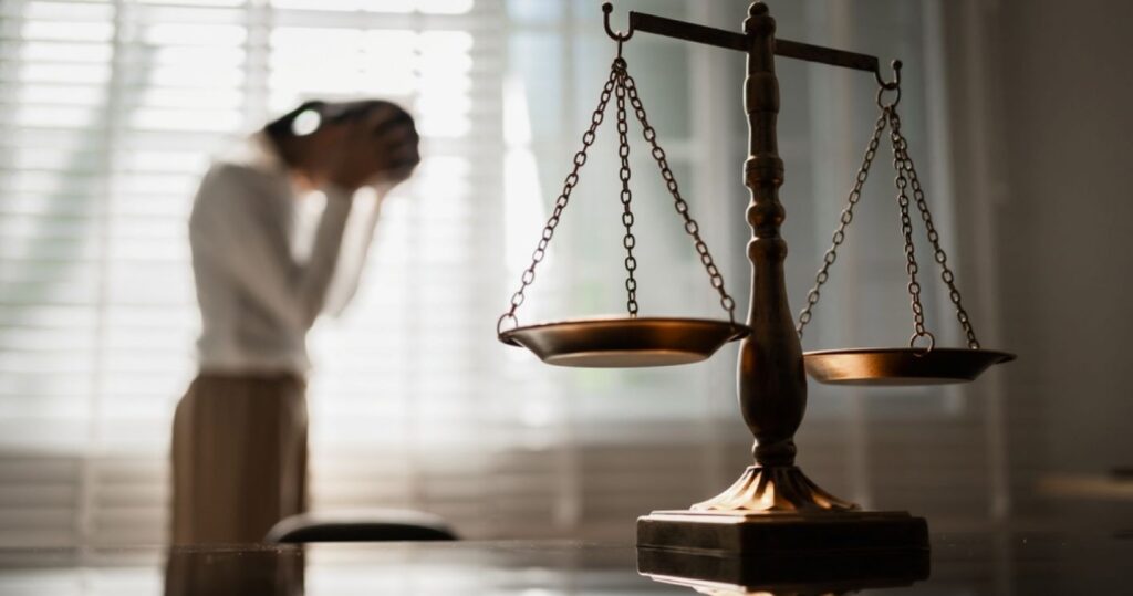 A Scales of Justice in the foreground with a blurry woman crying in the background.